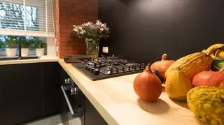 Ścianę między dolnymi i górnymi szafkami w kuchni pomalowano odporną na wilgoć farbą w kolorze czarnym.