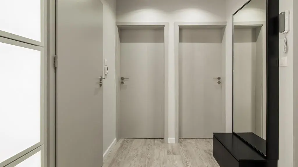 Szare drzwi w połączeniu z czarną szafką i lustrem w ramie w tym samym kolorze oraz święcącym panelem tworzą bardzo elegancką, minimalistyczną całość.