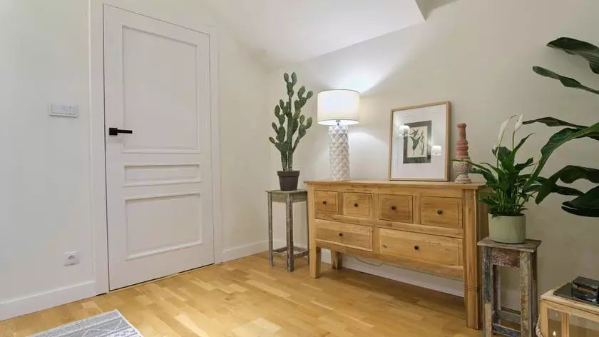 Zamiast dziury w ścianie - klasyczne drzwi, a zamiast minisiłowni - drewniana konsolka i rośliny. Do takiej sypialni przyjemnie się wchodzi!