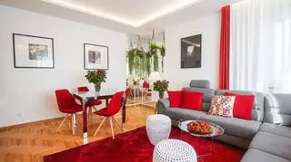 W salonie z szarością i bielą kontrastują czerwone dodatki: krzesła, dywan, poduszki i zasłony.