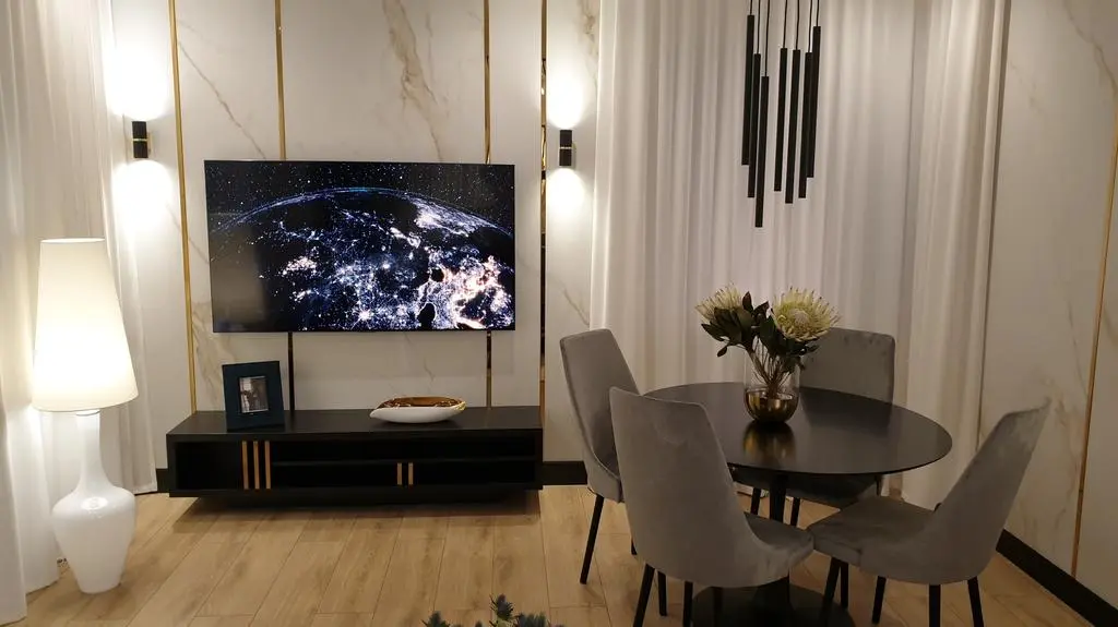 Ściana wyłożona wielkoformatowym gresem ozdobionym złotymi profilami stała się tłem dla telewizora i szafki medialnej.